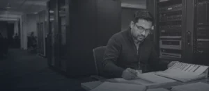 Bank technology engineer reviewing printed system documentation beside server racks