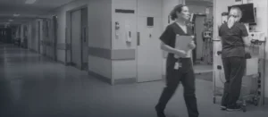 Clinical staff moving through a hospital corridor, one working at a wall-mounted workstation