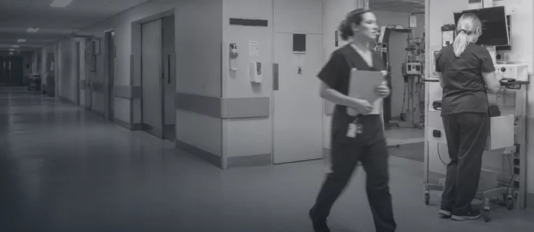 Clinical staff moving through a hospital corridor, one working at a wall-mounted workstation